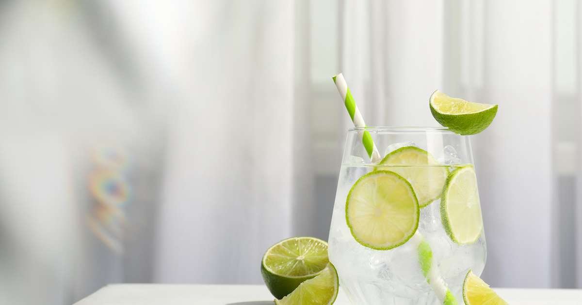 Copo de água com limão ao lado de fatias de limão fresco