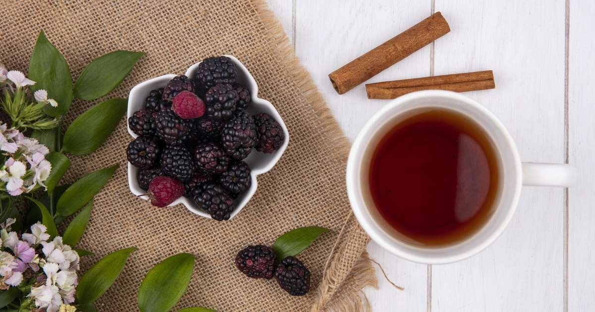 Preparação do chá de amora em uma xícara com folhas de amora ao lado