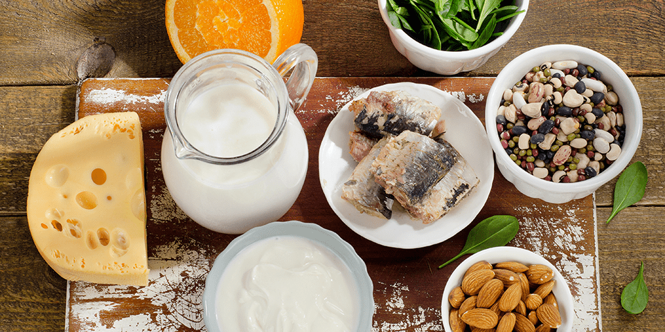 Diversos alimentos ricos em cálcio, como laticínios, vegetais verdes e frutos do mar, dispostos em uma mesa saudável.